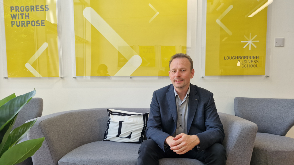 A person in a suit is sitting on a gray couch in front of three yellow posters.